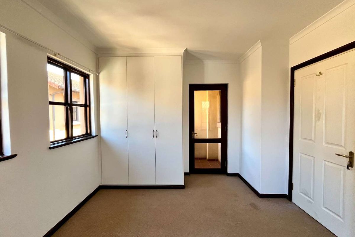 A vacant bedroom featuring built-in cupboards, carpeted flooring, and a glass-panelled door leading to an adjacent space.