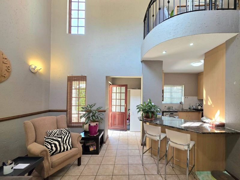 Open plan living area featuring a double-volume ceiling, mezzanine level with wrought iron railing, tiled floors, and a functional kitchen with granite countertops.
