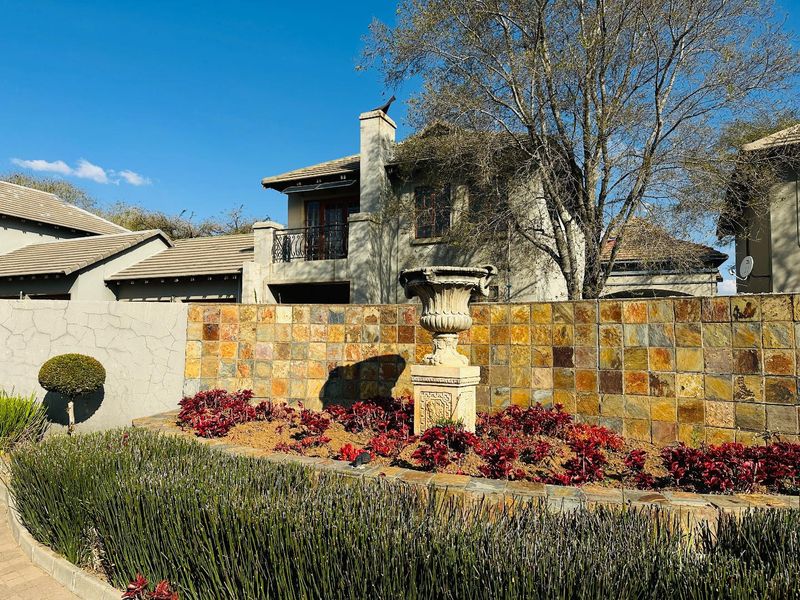 Front view of a townhouse featuring a stone-tiled boundary wall, landscaped garden with a decorative stone urn, and a multi-story structure with a tiled roof.