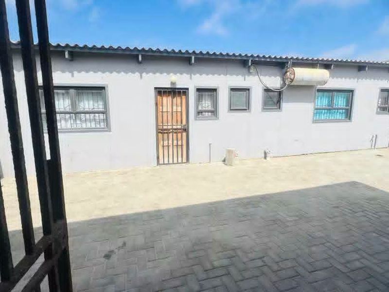A paved rear courtyard area featuring a single-story building facade with security gates, window bars, and an external electric geyser.