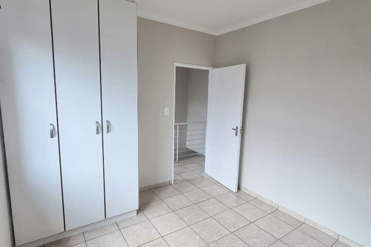 A bright, empty bedroom featuring built-in cupboards, neutral tiled flooring, and direct access to a hallway.