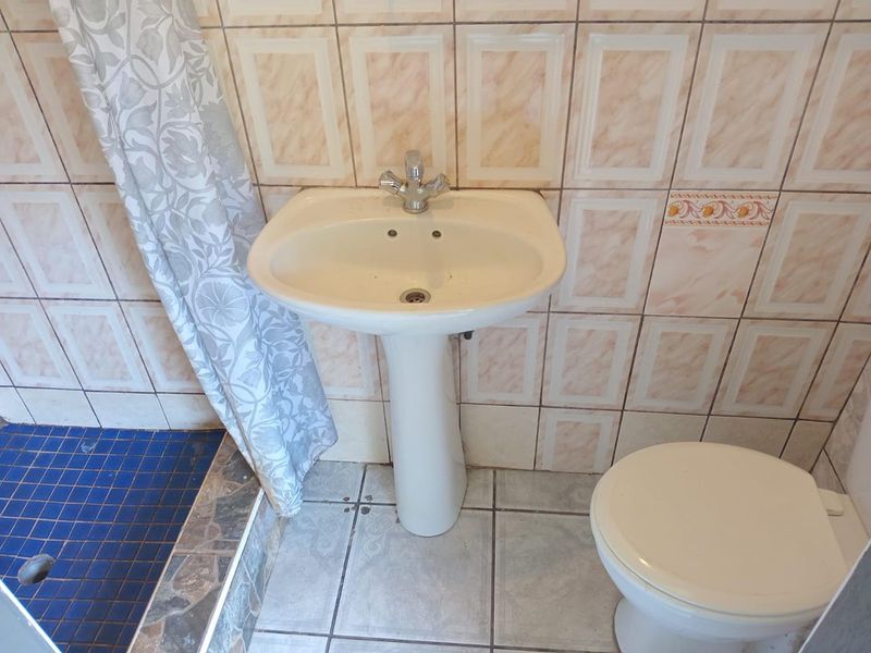 A dated bathroom featuring a pedestal basin, toilet, and shower area with tiled finishes, requiring modernization to improve its aesthetic appeal.