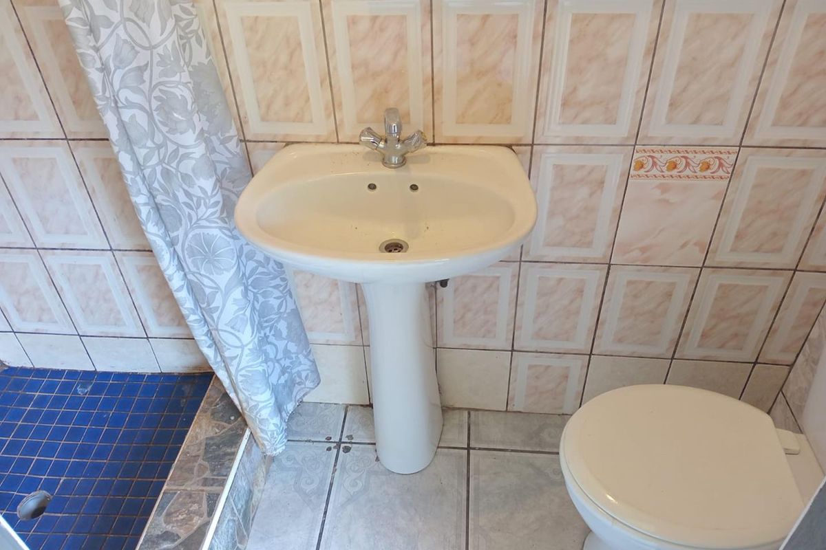 A dated bathroom featuring a pedestal basin, toilet, and shower area with tiled finishes, requiring modernization to improve its aesthetic appeal.