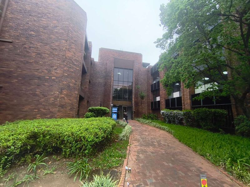Front exterior view of a multi-story brick office building featuring a paved walkway and established garden landscaping.