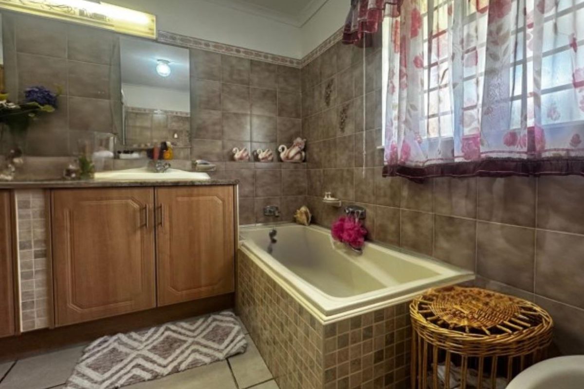 A functional bathroom featuring a built-in bathtub with tiled surround, vanity cabinet with integrated basin, and wall-mounted mirror.