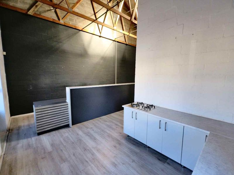 Industrial style kitchen area featuring exposed timber roof trusses, modern white cabinetry, and a built-in gas cooktop.