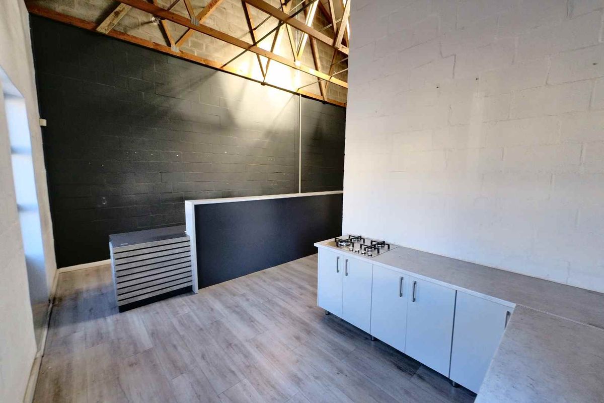 Industrial style kitchen area featuring exposed timber roof trusses, modern white cabinetry, and a built-in gas cooktop.