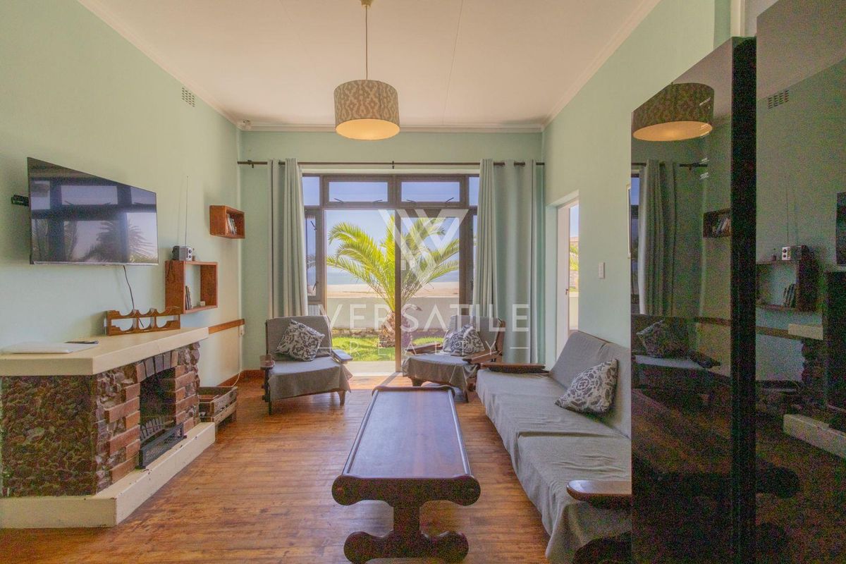 A living room featuring a brick fireplace, wood-look flooring, and sliding glass doors that open to an outdoor area with sea views.