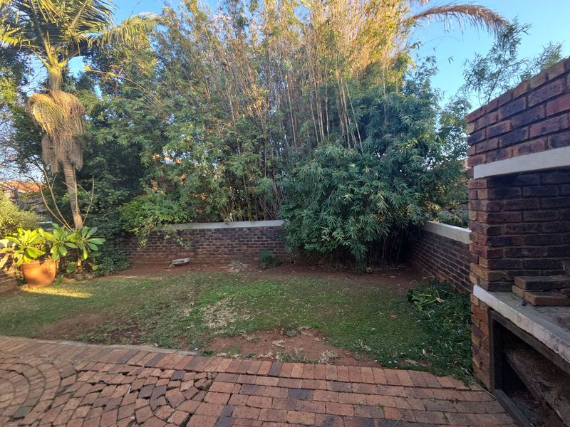 Private rear garden featuring a built-in brick braai, paved patio area, and established perimeter walling with mature greenery.