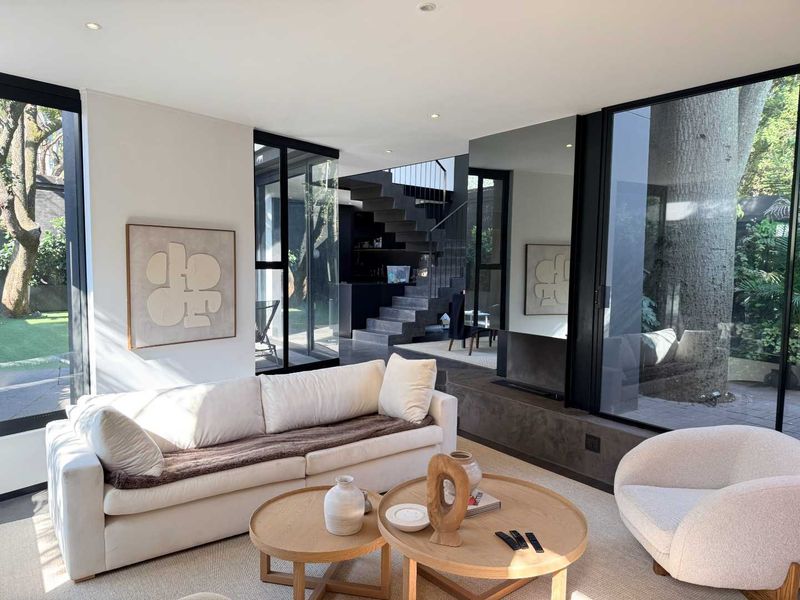 Modern living room featuring floor-to-ceiling windows, a built-in fireplace with a concrete hearth, and an architectural staircase.