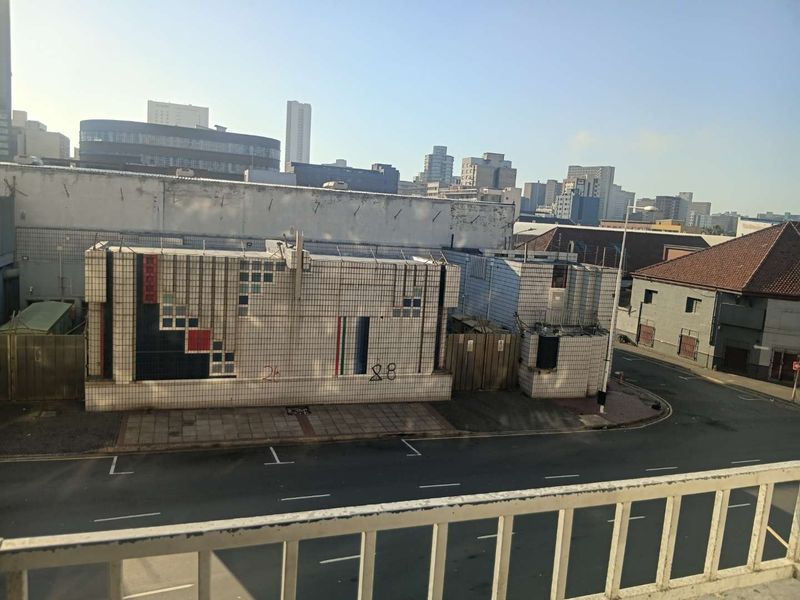 An elevated urban view overlooking a street and neighboring commercial buildings with tiled facades and city skyline in the background.