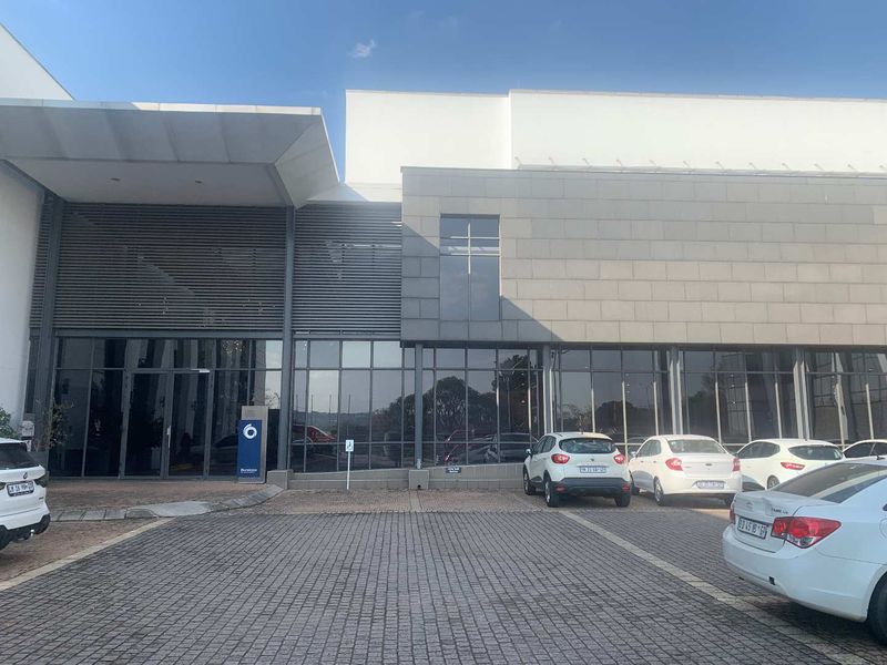 Modern office building exterior featuring a glass curtain wall facade, stone cladding, and a paved parking area with a covered entrance.