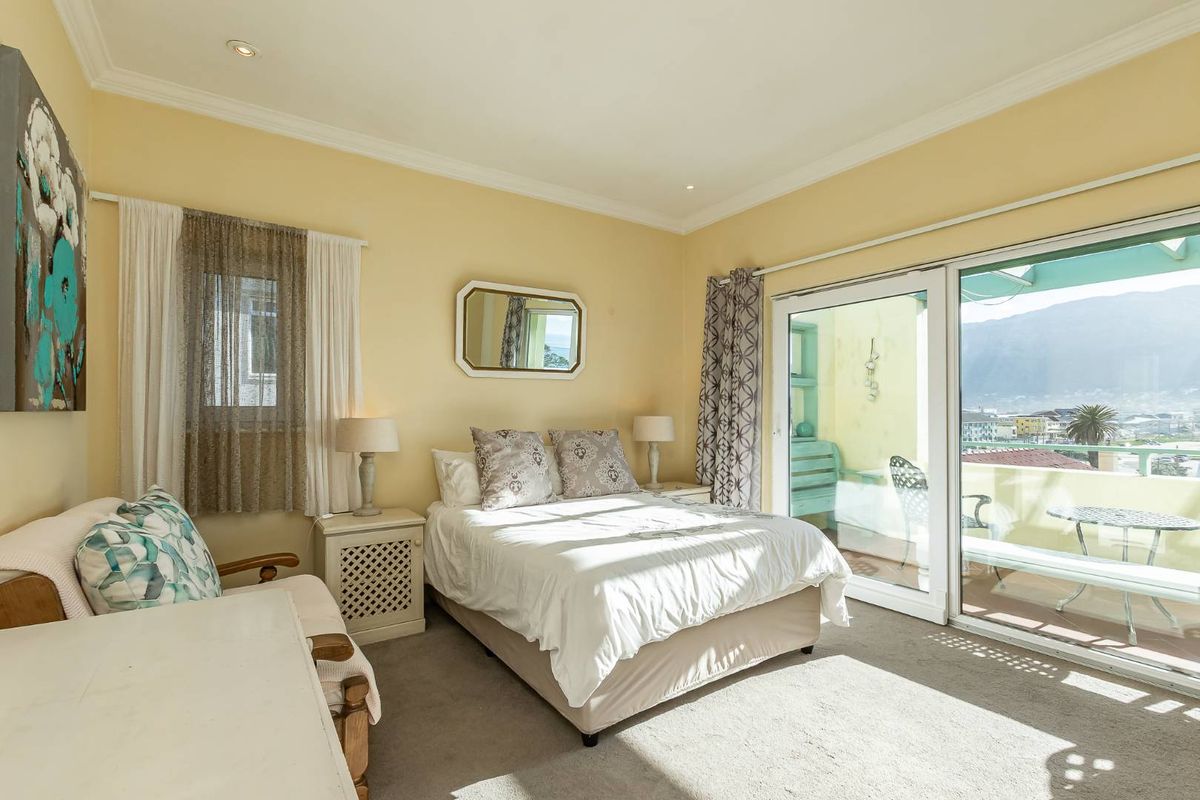 A bright bedroom featuring neutral walls, carpeted flooring, and large sliding glass doors that open onto a private balcony with scenic views.