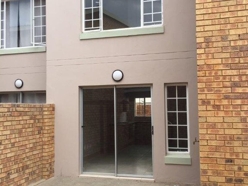 Rear view of the townhouse featuring a paved patio area, sliding glass door access, and brick boundary walling.