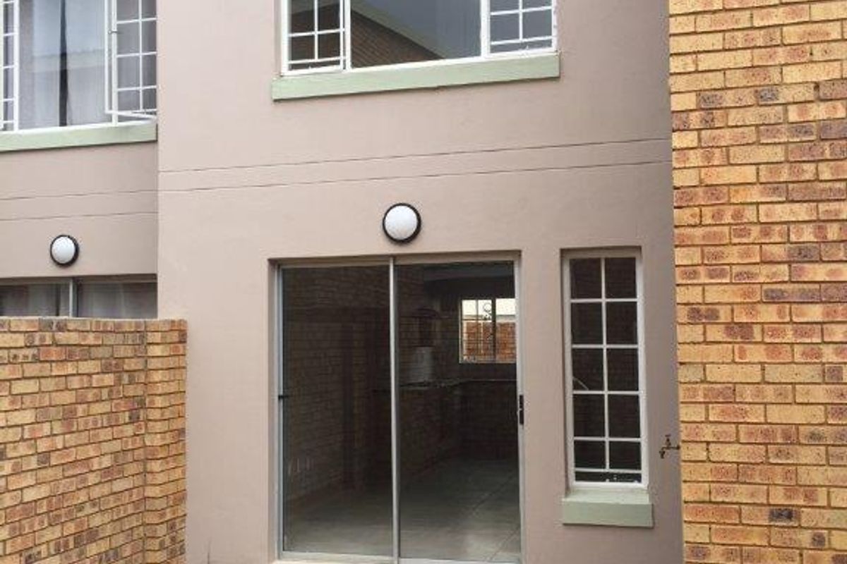 Rear view of the townhouse featuring a paved patio area, sliding glass door access, and brick boundary walling.