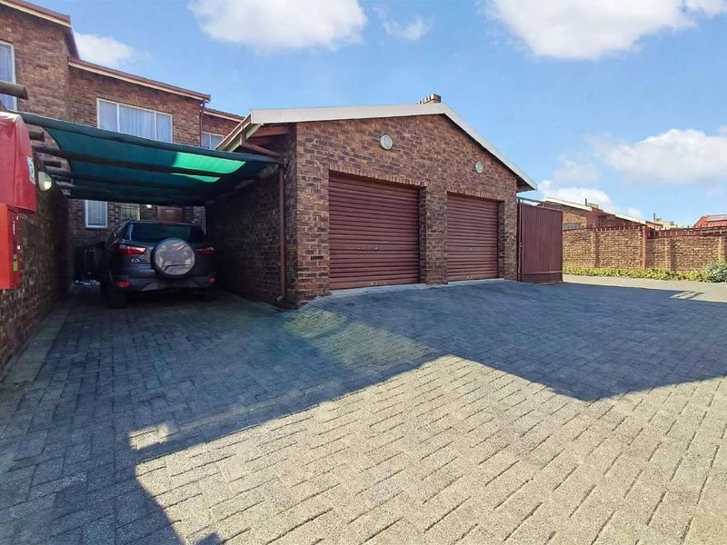 Exterior view of a townhouse featuring a double garage with roll-up doors, an attached carport, and a paved driveway.