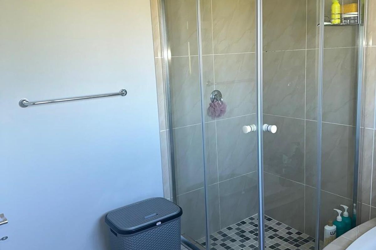 A functional bathroom featuring a glass-enclosed shower with tiled walls and a mosaic-tiled shower floor, complemented by a wall-mounted towel rail.