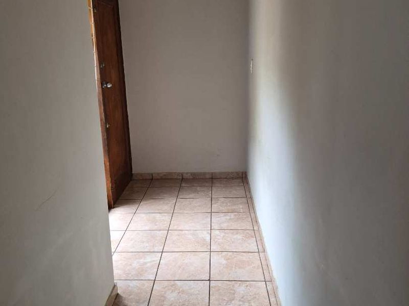A simple, empty hallway featuring neutral tiled flooring and a wooden door, providing a clean transition space within the home.