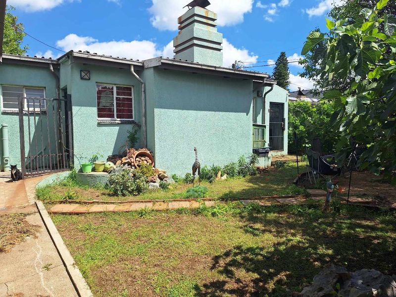 Rear view of the property featuring a prominent chimney, plastered exterior walls, and a garden area with a concrete pathway.