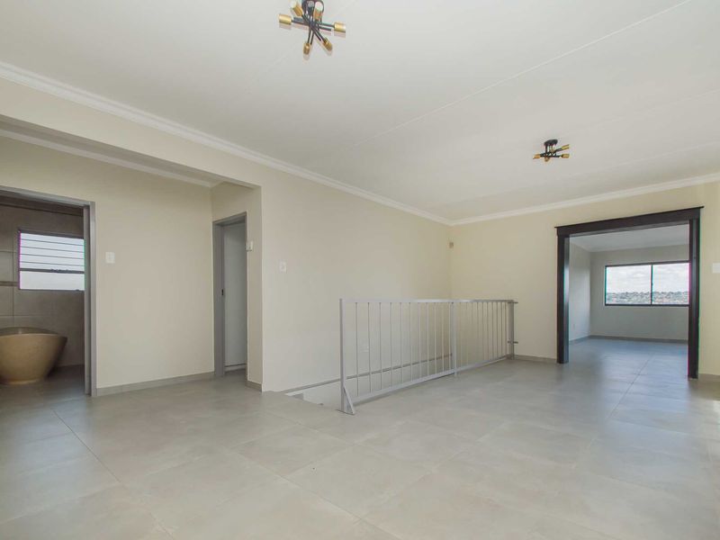 A spacious, empty landing area featuring neutral tiled flooring, modern light fixtures, and a metal stair railing, providing access to adjacent rooms.