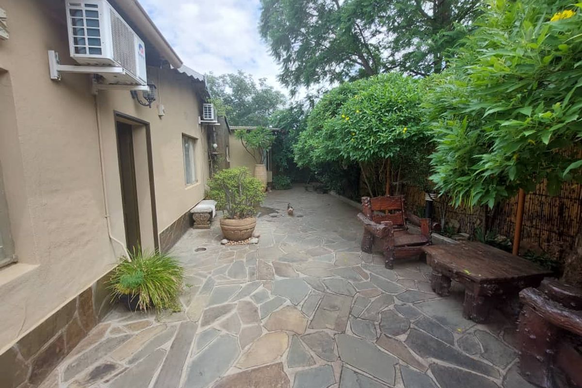 A paved rear courtyard area featuring stone flooring, exterior wall-mounted air conditioning units, and established garden landscaping.