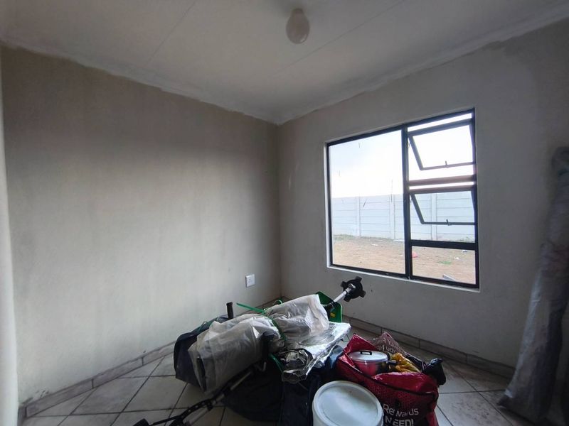 A vacant bedroom featuring tiled flooring and an aluminium window frame, currently requiring finishing touches to the wall surfaces.