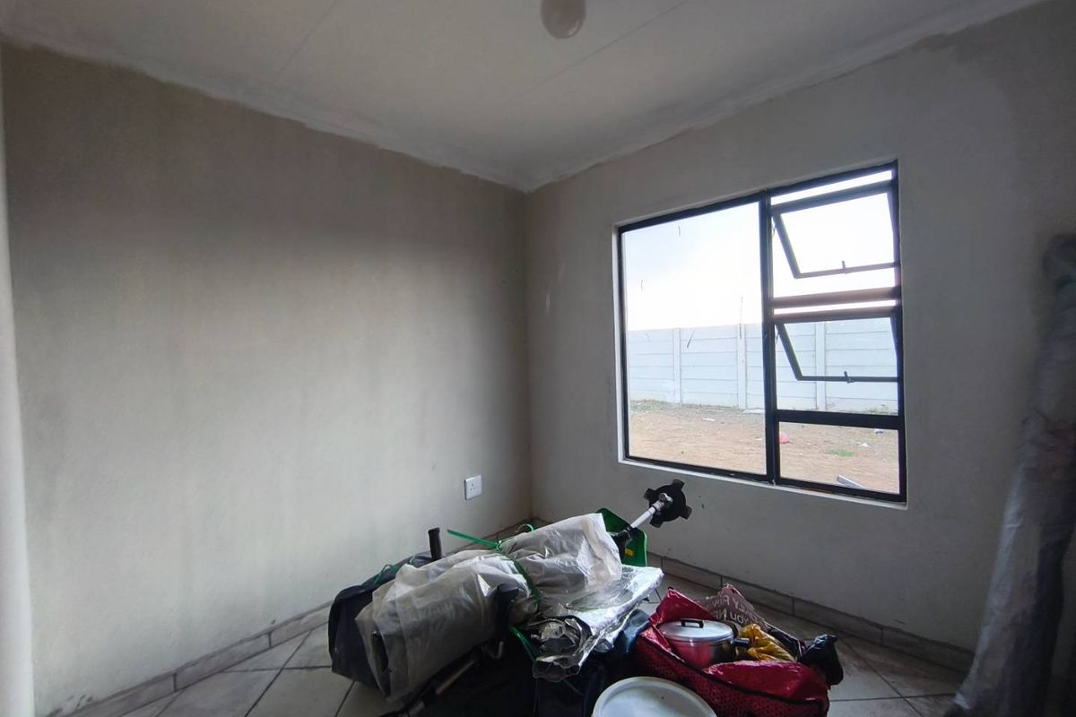 A vacant bedroom featuring tiled flooring and an aluminium window frame, currently requiring finishing touches to the wall surfaces.