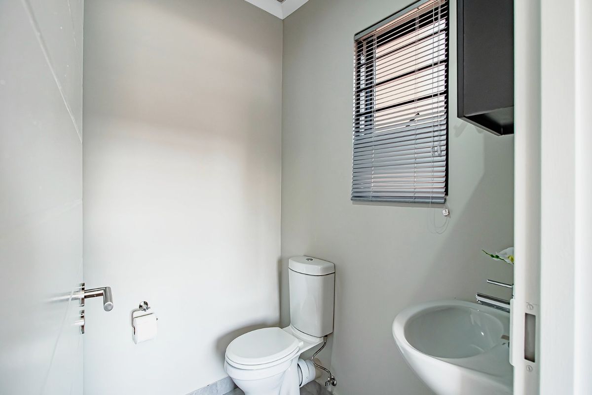 A clean and functional guest bathroom featuring a modern toilet, pedestal washbasin, and venetian blinds for privacy.