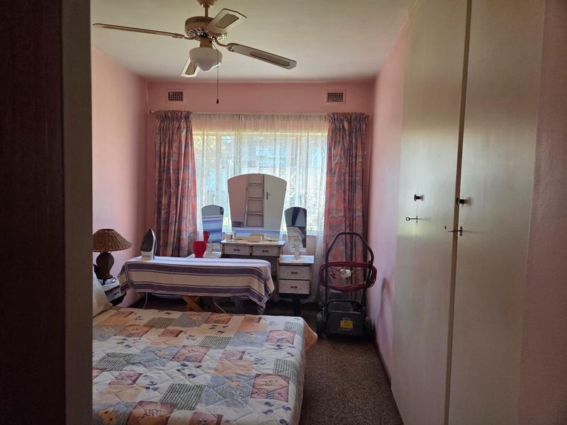 A bedroom featuring built-in cupboards, carpeted flooring, and a ceiling fan, offering a functional space with potential for modernization.