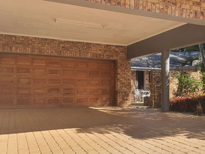 A spacious covered carport area featuring a classic wooden garage door and durable brick construction, providing secure parking and a sheltered entrance.