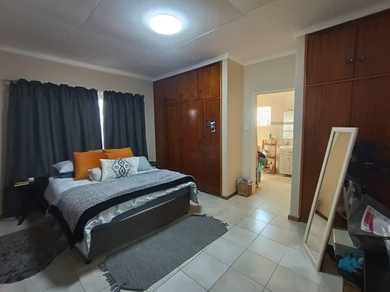 A bedroom featuring built-in wooden cupboards, tiled flooring, and an adjoining bathroom entrance.