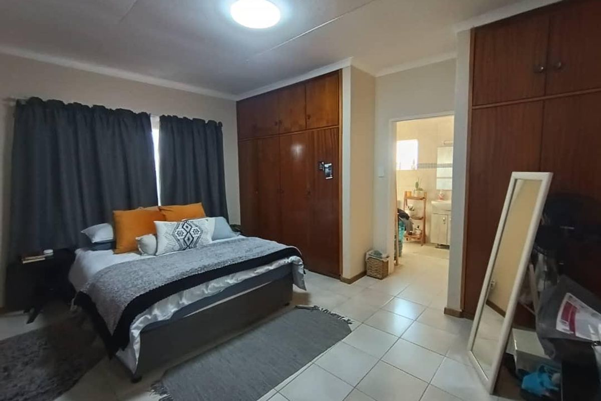 A bedroom featuring built-in wooden cupboards, tiled flooring, and an adjoining bathroom entrance.
