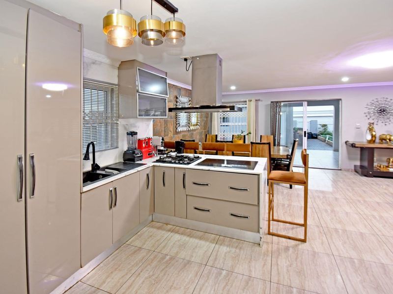 Modern open-plan kitchen featuring sleek cabinetry, integrated hob and cooktop, extractor fan, and tiled flooring, flowing seamlessly into the dining and living areas.