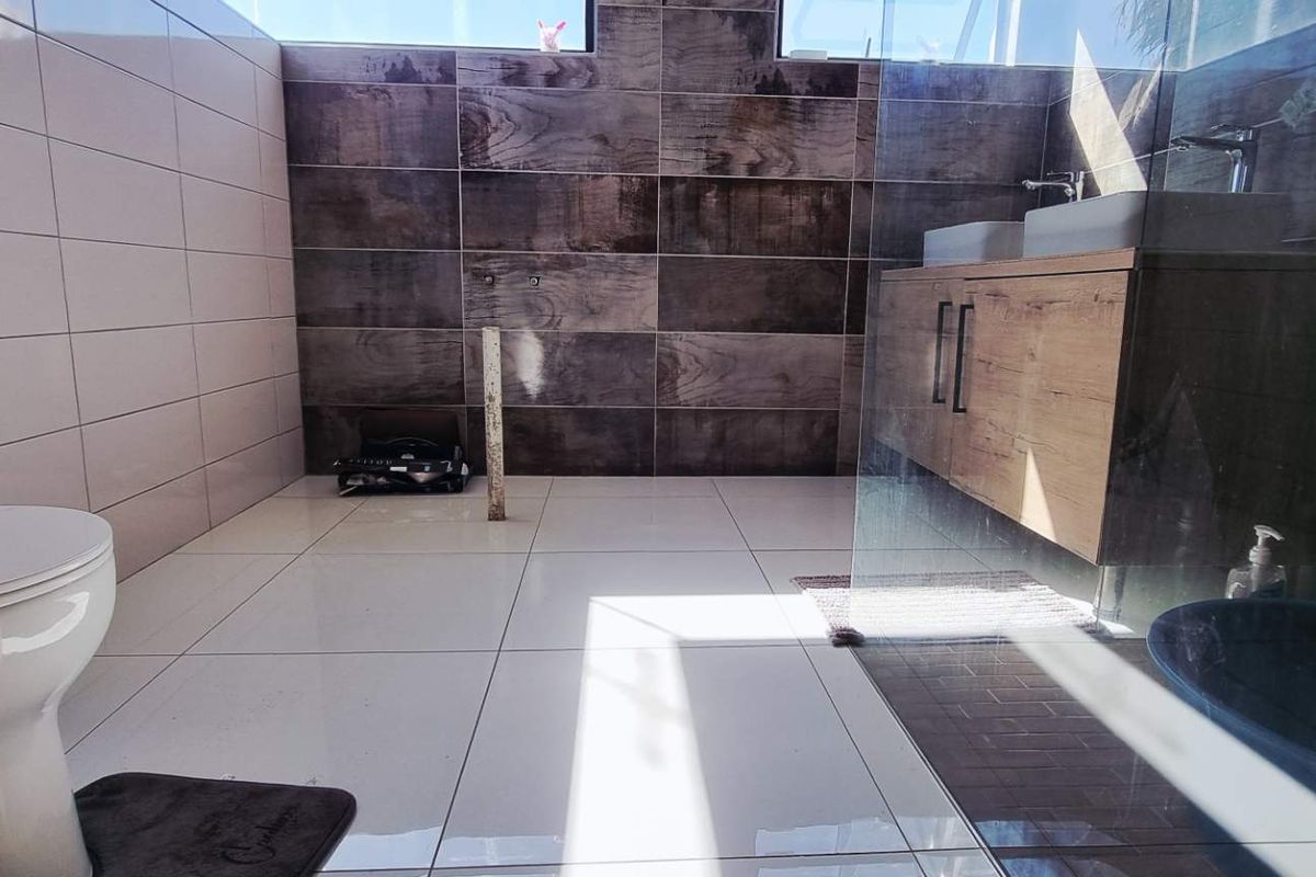 Modern bathroom featuring dual vanity with wood-look cabinetry, large format floor tiles, and a glass-enclosed shower area.