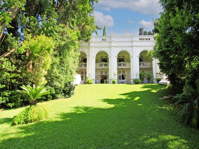 A view of the rear elevation of the guest house, featuring a grand double-story arched veranda overlooking a lush, well-maintained garden.