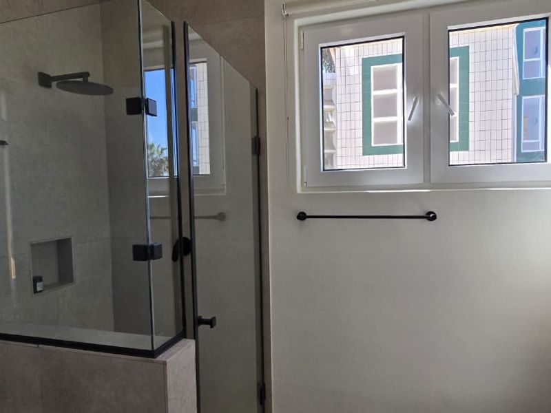 Modern bathroom featuring a glass-enclosed walk-in shower with a rain shower head, recessed niche, and a bright window for natural light.