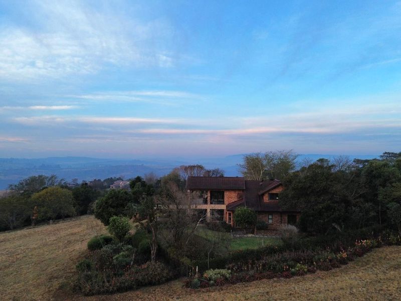 An aerial view of a brick-faced house set within a large, landscaped garden with expansive rural views.
