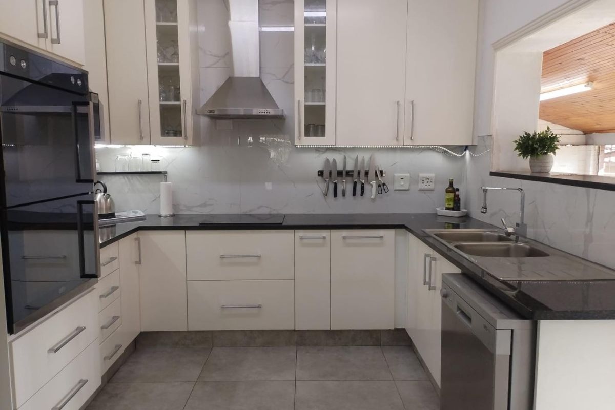 Modern kitchen featuring white cabinetry, stone countertops, a built-in oven, extractor fan, and a double sink with a tiled backsplash.