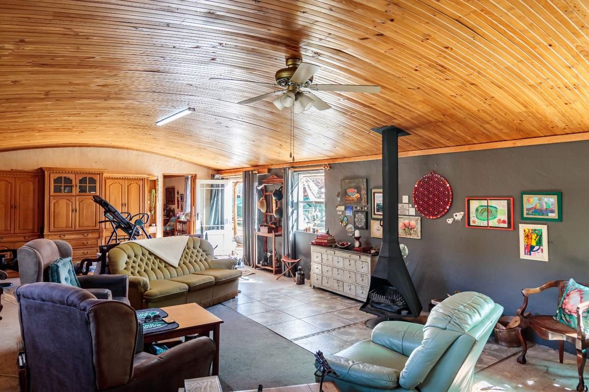 Spacious living room featuring a vaulted timber ceiling, tiled flooring, and a prominent freestanding fireplace, offering a rustic and cozy atmosphere.
