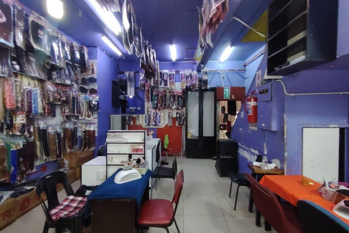 Interior view of a retail space featuring tiled flooring, fluorescent lighting, and wall-mounted shelving, currently utilized as a hair and beauty supply shop.