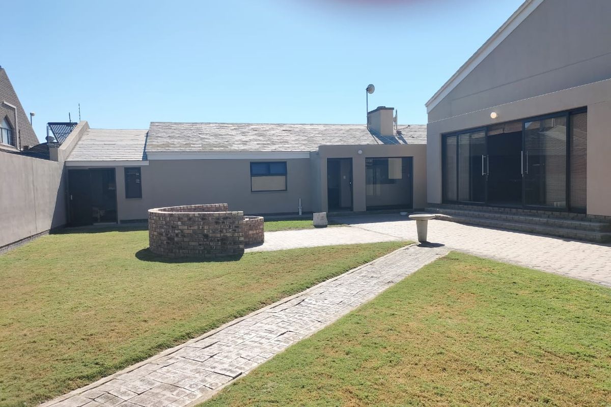 A spacious rear courtyard featuring a paved patio area, a circular brick fire pit, and a landscaped garden with a stone pathway.