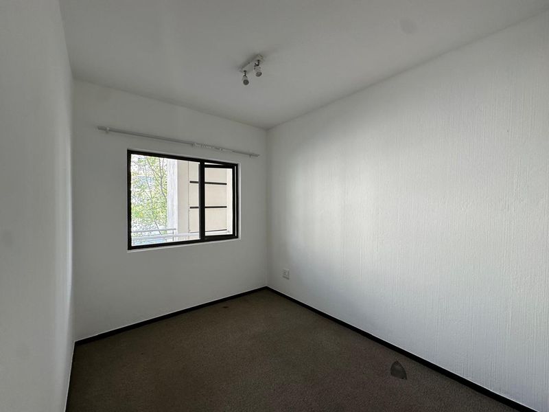 An empty bedroom featuring neutral walls, carpeted flooring, and a window providing natural light.