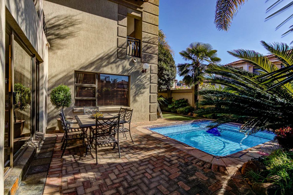 Rear exterior view featuring a brick-paved patio area, a swimming pool with safety net, and access to the home via sliding glass doors.