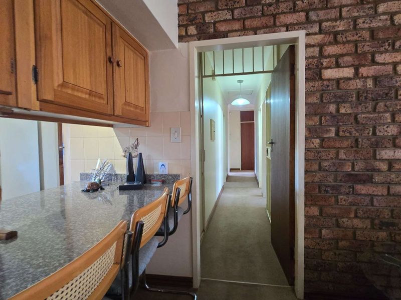 Kitchen area featuring a granite breakfast bar, wooden cabinetry, and a distinctive exposed brick wall leading into a hallway.