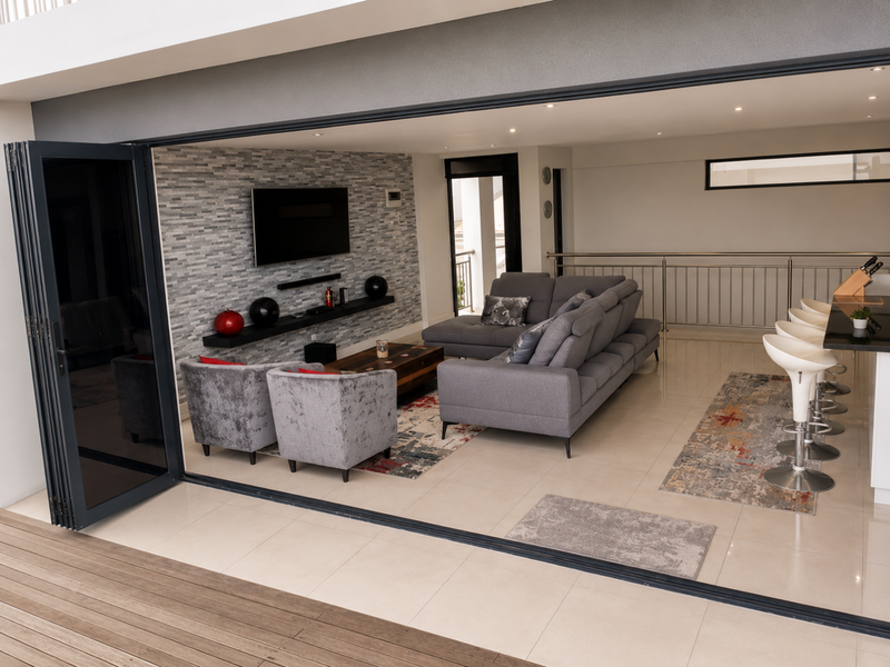 Modern open-plan living area featuring a stone feature wall, sleek porcelain tiling, and large stacking doors that open onto an outdoor deck.