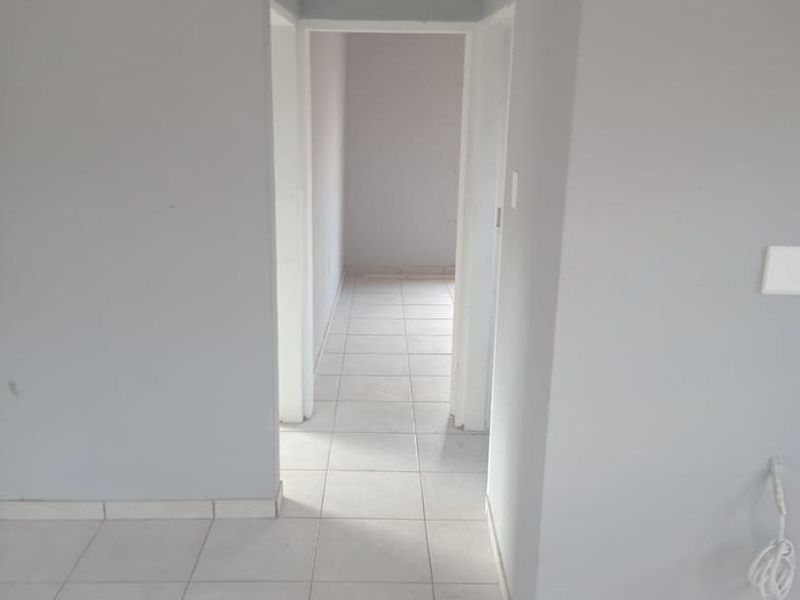 A clean, empty hallway featuring neutral grey walls, white tiled flooring, and classic coving detail, providing a bright and simple transition space.