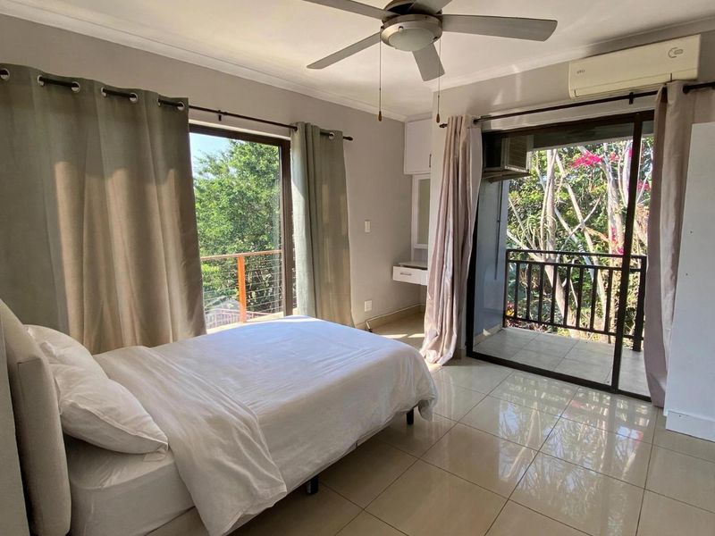 Bright bedroom featuring tiled flooring, a ceiling fan, air conditioning, and dual sliding glass doors opening onto a private balcony with garden views.