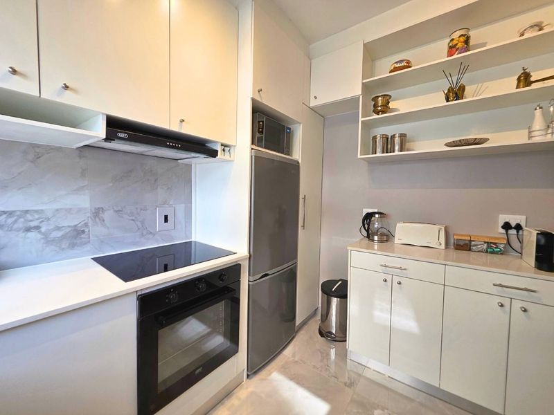 Modern kitchen featuring sleek white cabinetry, stone countertops, integrated appliances including an oven and hob, and stylish marble-look splashback tiling.