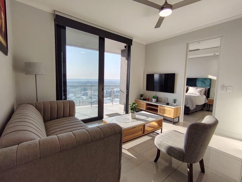 Modern living room featuring tiled floors, a ceiling fan, and large sliding glass doors leading to a balcony with expansive views.
