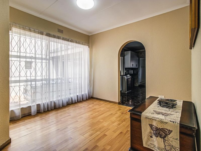 A bright, empty living room featuring laminate flooring, an arched doorway leading to the kitchen, and a large window with security bars.